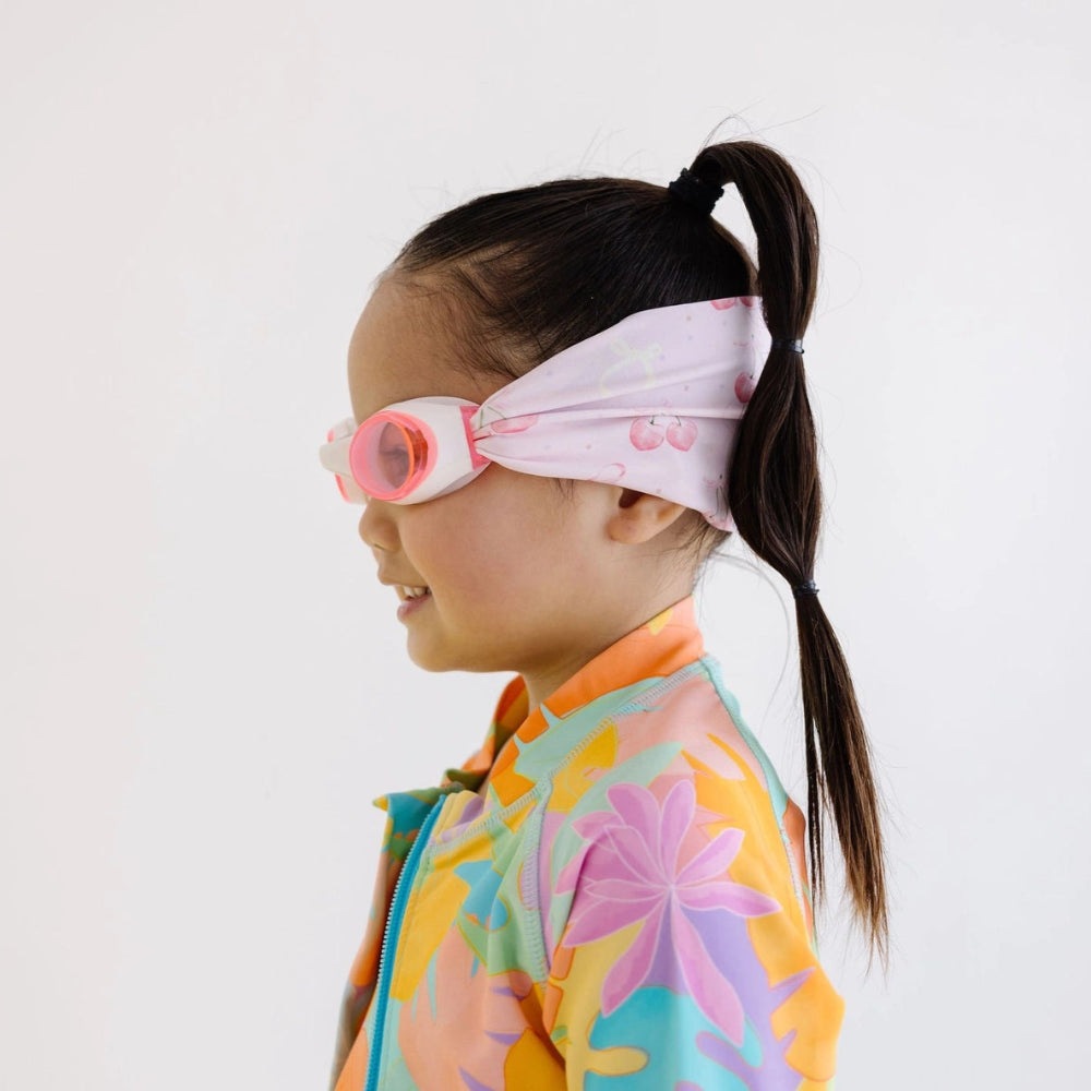 Splash Swim Goggles Cherry Charms pink-framed goggles worn by a child in a bright floral swimsuit