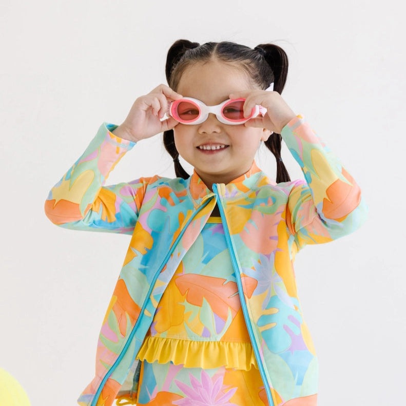 Splash Swim Goggles Cherry Charms kids goggles with pink and white frame worn by a smiling child in a colorful outfit.