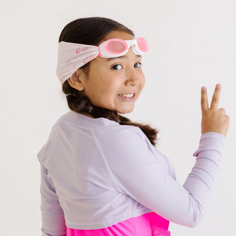 Splash Swim Goggles Cherry Charms pink goggles worn by a smiling girl in a lavender top with a floral headband