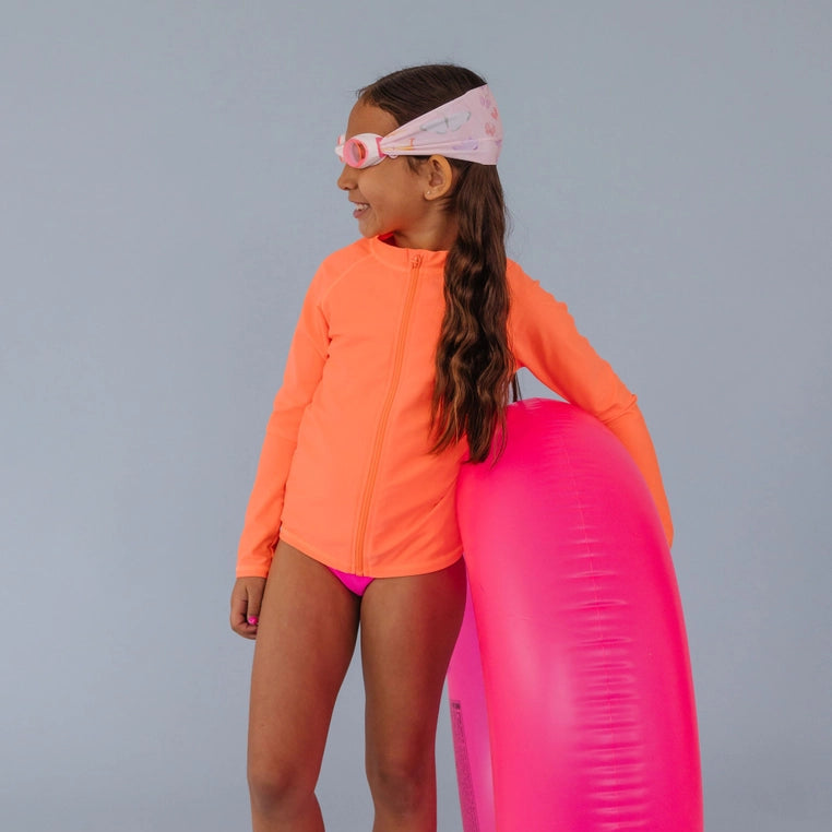 Splash Swim Goggles Flutter pink goggles worn by a girl in an orange swim top with a pink pool tube