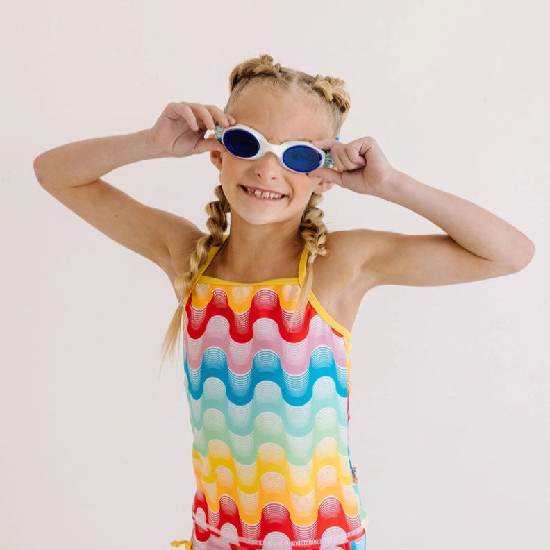 Splash Swim Goggles Sea Glass with blue lenses worn by smiling girl in a rainbow wavy swimsuit