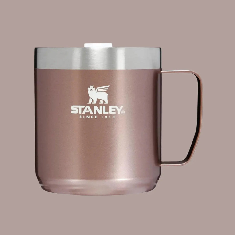 Stanley Classic Stay-Hot Camp Mug 12 oz in rose-gold with stainless lid, gripped by its curved handle.