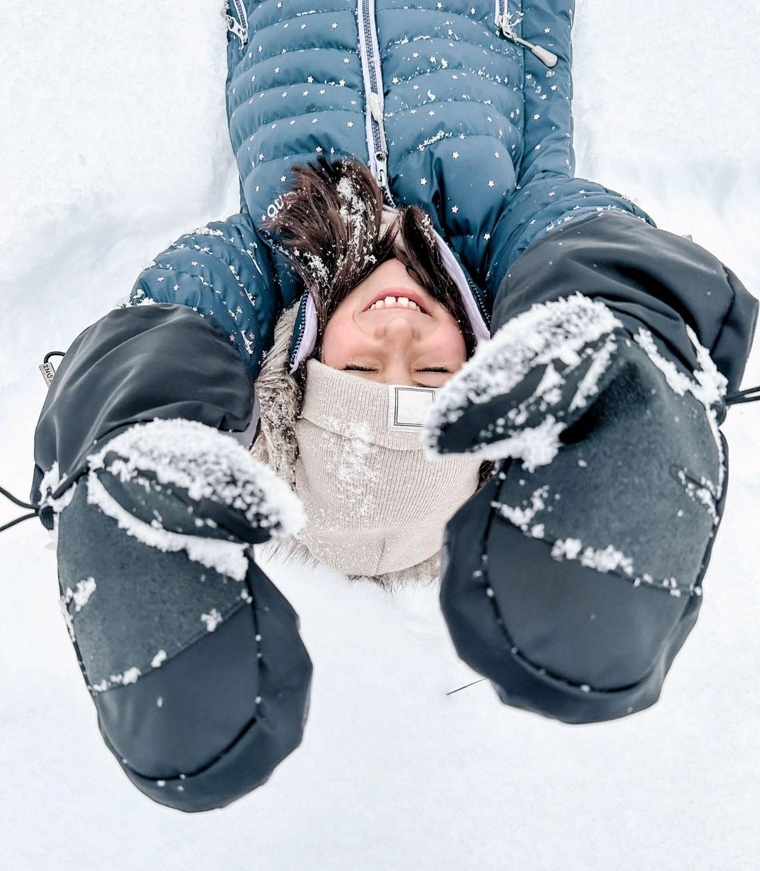 Child wearing Stonz Black/Grey Snow Mitts while playing in the snow in a blue winter jacket.