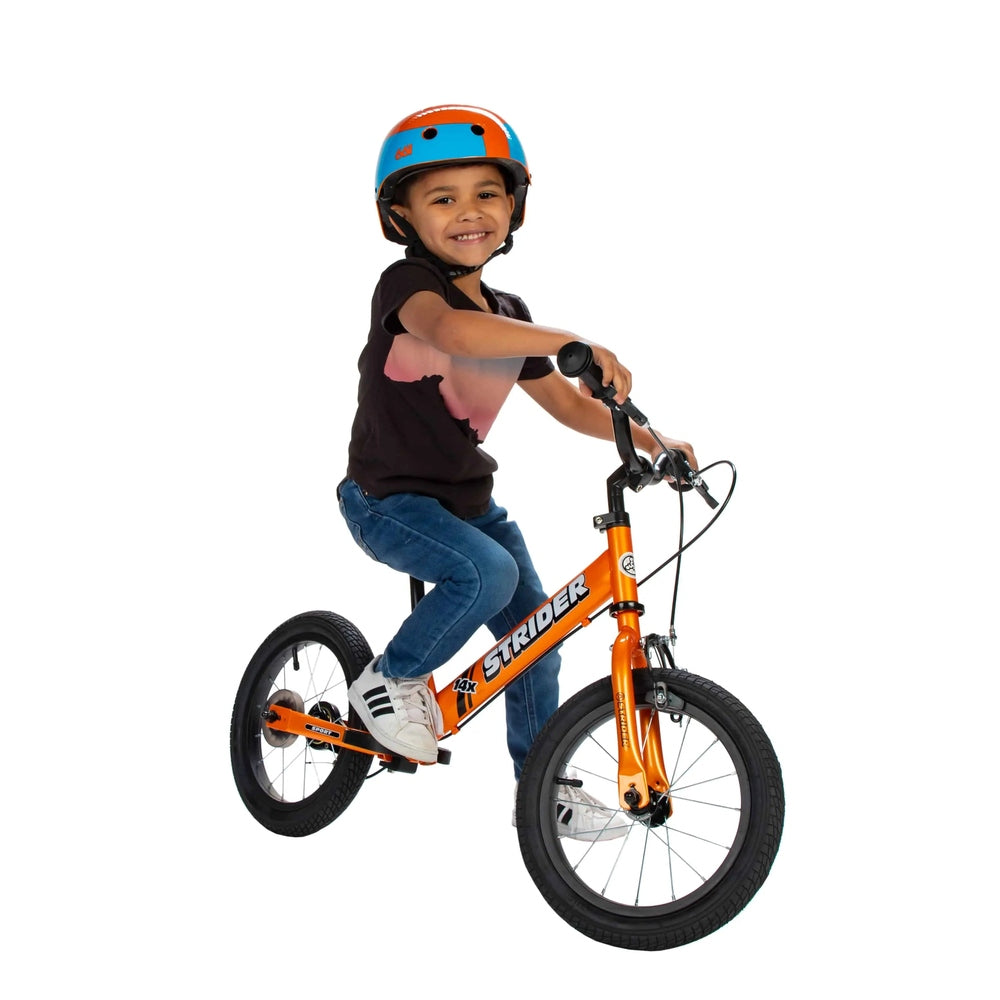 Strider 14X Sport Balance Bike orange frame; cheerful child rides it wearing a blue-and-orange helmet.