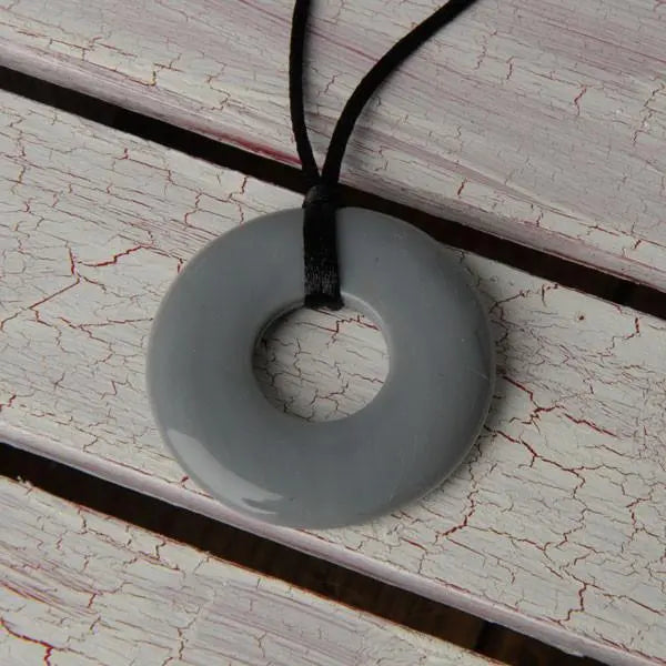 Teethease Original Pendant, gray donut teething pendant on black cord, resting on weathered wood.