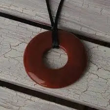 Teethease Original Pendant brown donut-shaped necklace on black cord resting on weathered wood.