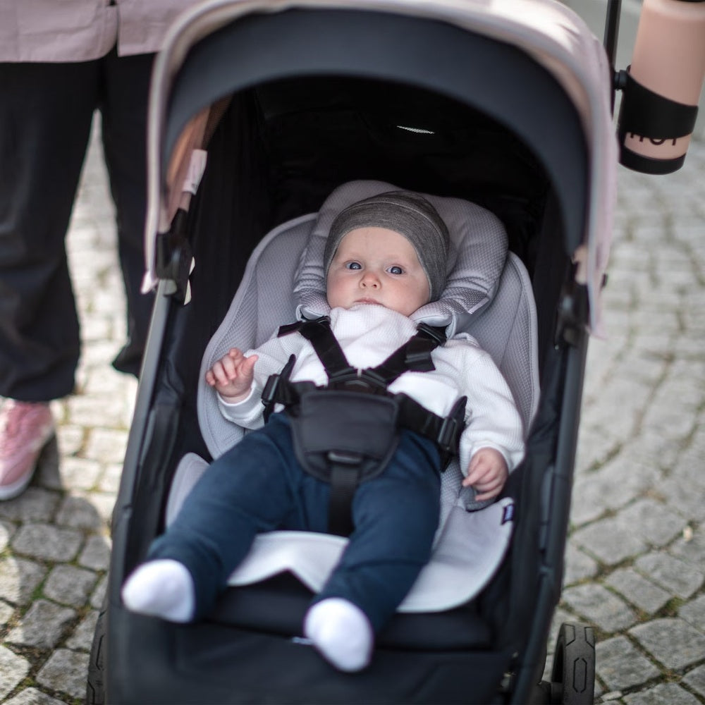 Thule newborn inlay gray stroller insert for infant support inside a gray stroller with a baby.
