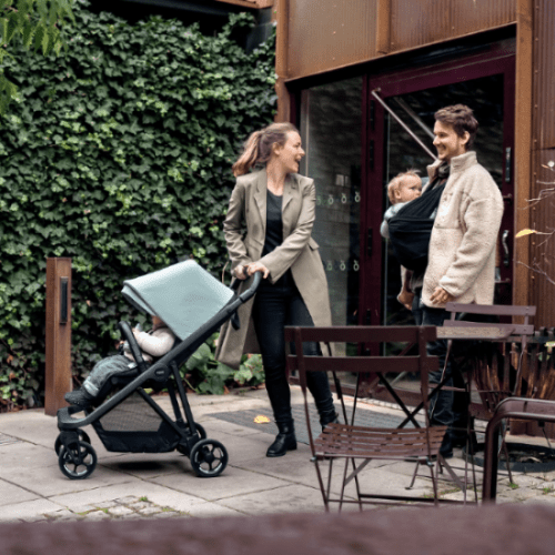 Thule Shine stroller with light gray canopy and black frame, outdoors with a mother pushing and a father carrying a baby
