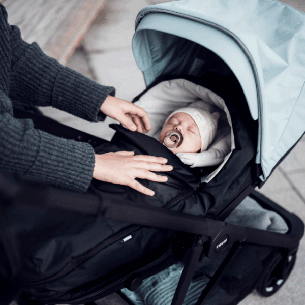 Thule Shine baby stroller with light blue canopy and infant in white hat with pacifier
