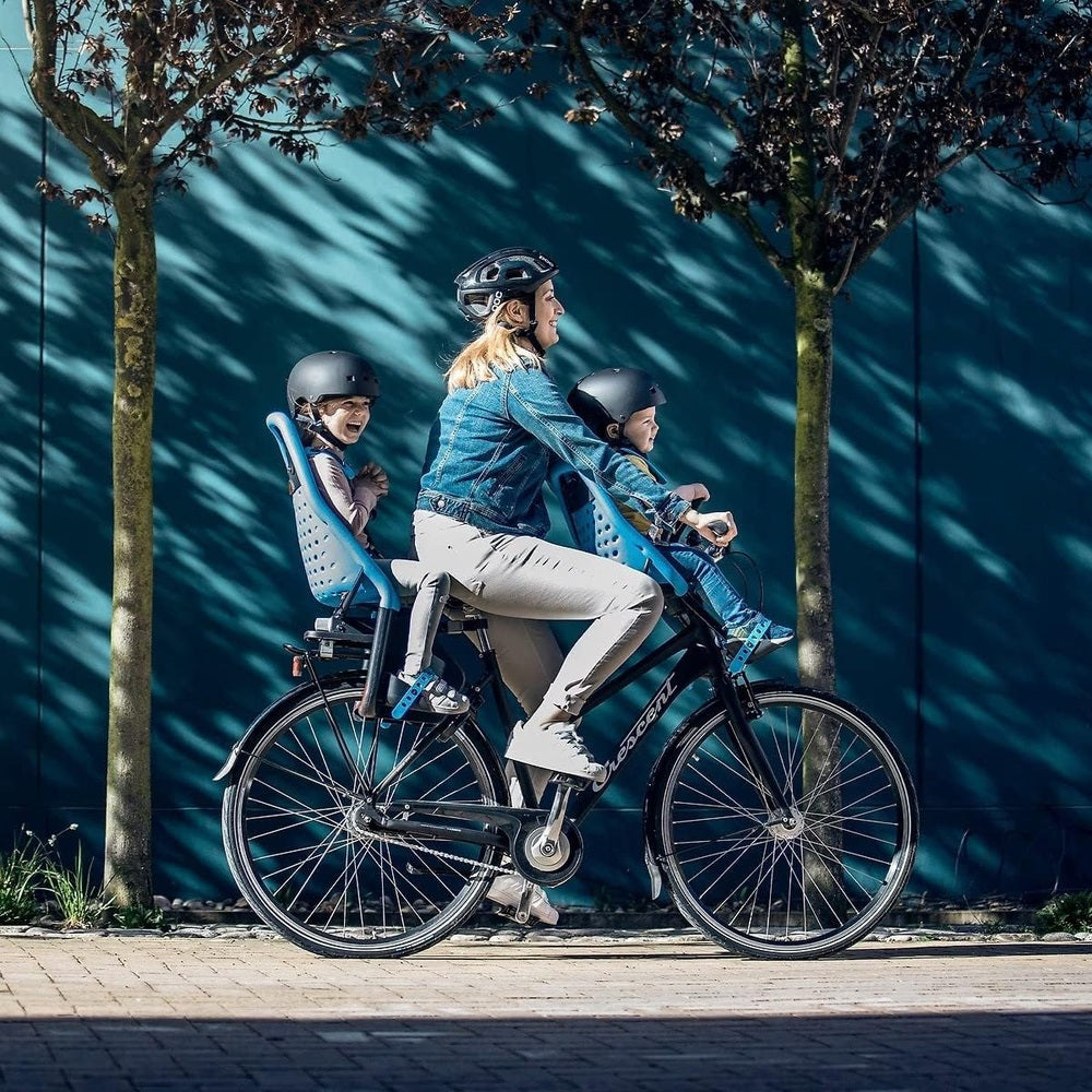 Thule Yepp Maxi rack-mounted child bike seats on a blue bike; a mom and two kids wear helmets while riding.