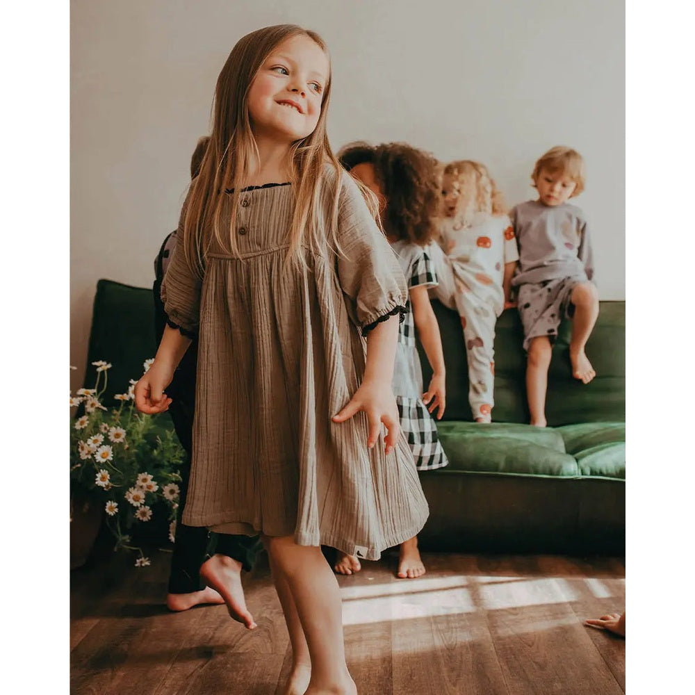 Turtledove London Herb Gauze Dress; beige, lightweight cotton; a toddler girl twirls happily in her dress.