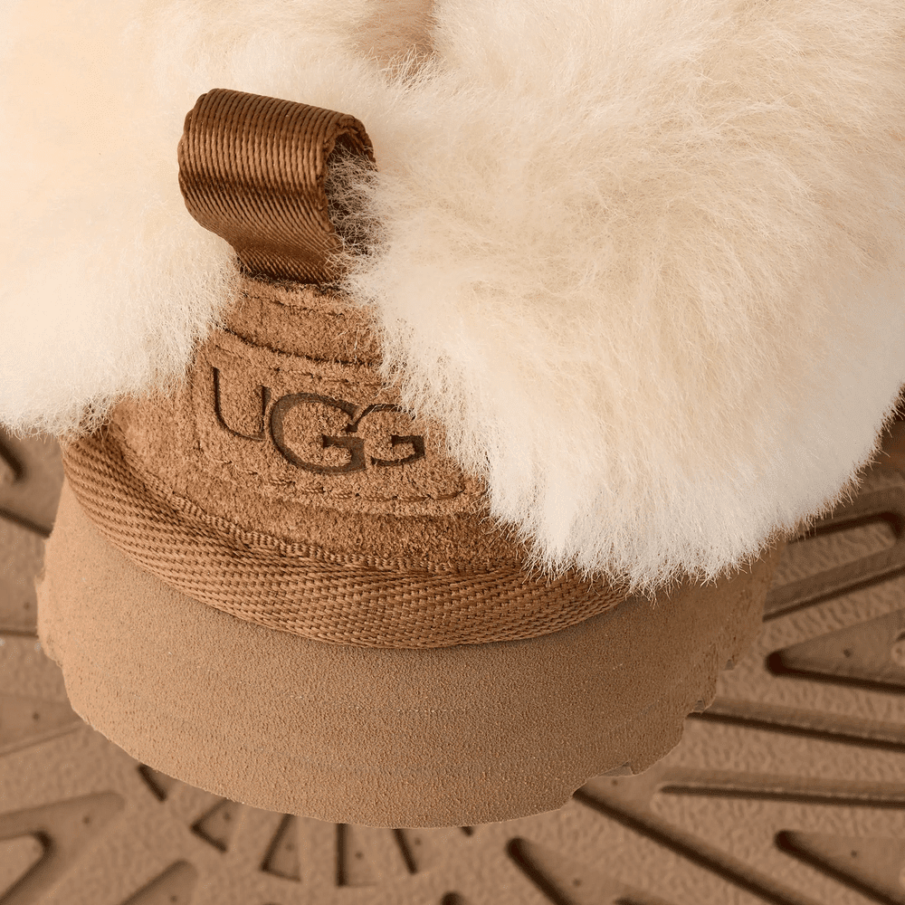 UGG Kids' Tazzelle Chestnut boot with plush shearling trim and tan suede, shown resting on a textured sole.
