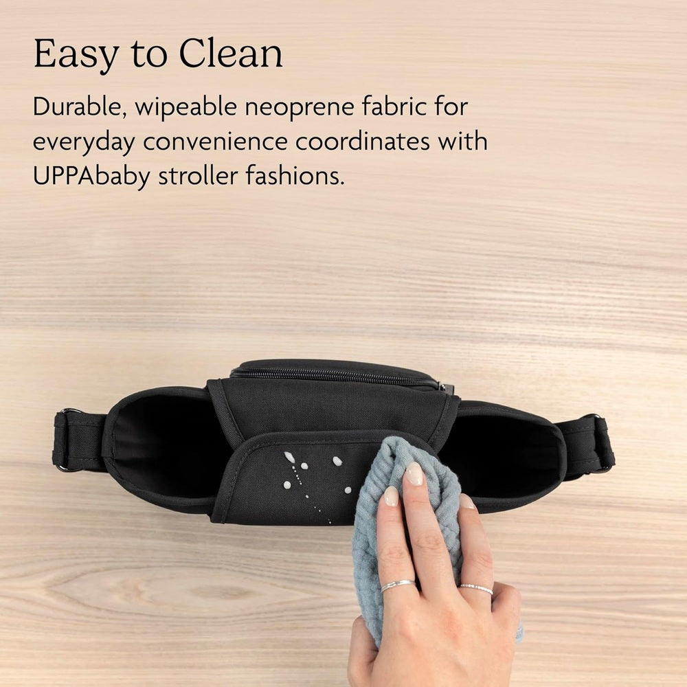 Black neoprene Uppababy Carry-All Parent Organizer with zip pocket and side straps, being wiped clean with gray cloth.