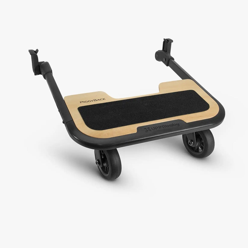 UPPAbaby Cruz PiggyBack ride-along board isolated on white, angled front view with wood platform, black non-slip surface, wheels, and stroller attachment arms.
