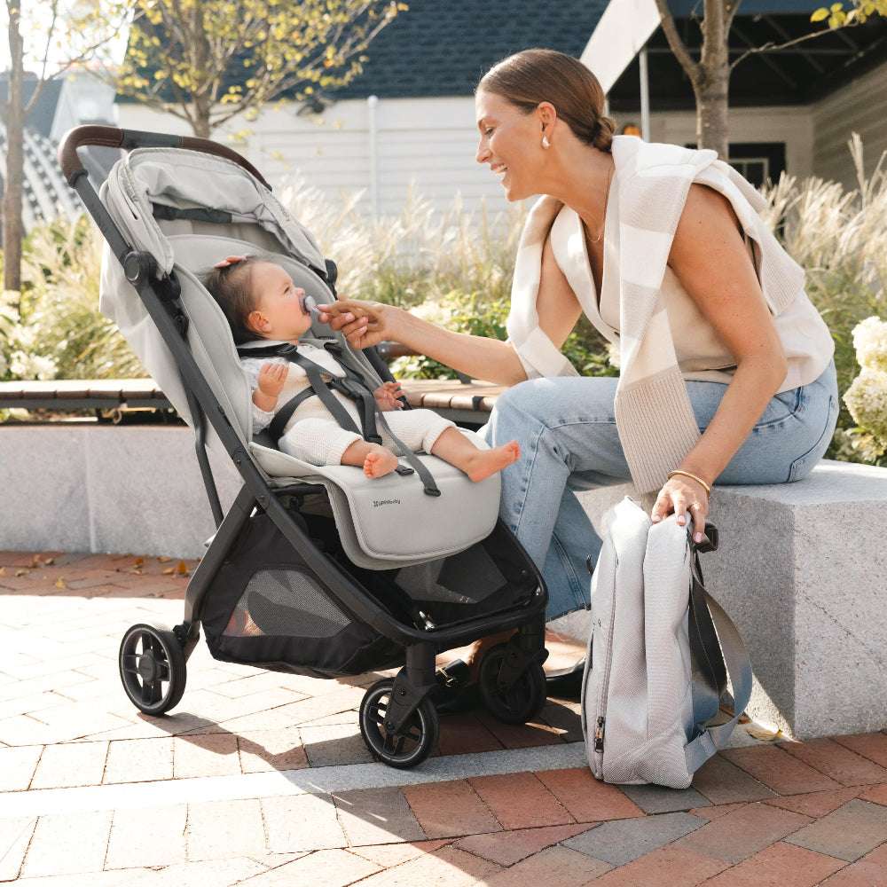 Uppababy Minu V3 stroller in gray with a baby secured in the harness beside caregiver