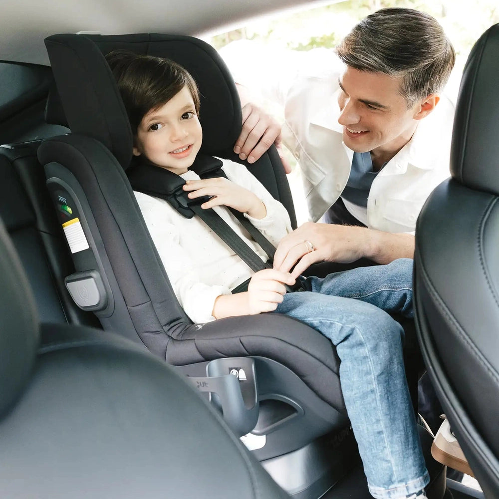 Uppababy Rove convertible car seat in black fabric; child buckling harness with caregiver beside in back seat
