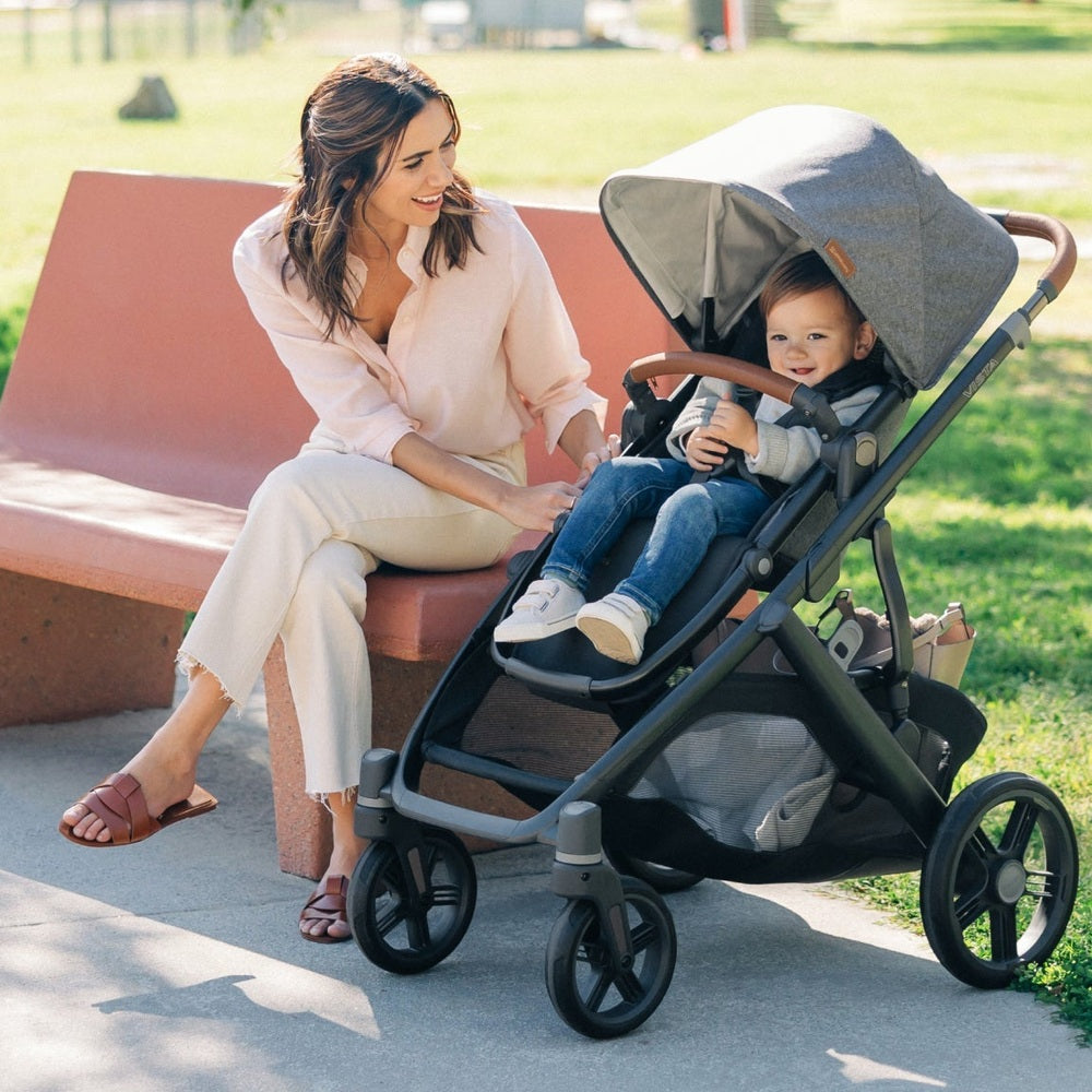 UPPAbaby Vista V3 stroller with caregiver and child resting on a bench in a park.
