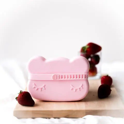 We Might Be Tiny Bear Snackie pink bear-shaped snack container with snap-lid resting on a board beside berries