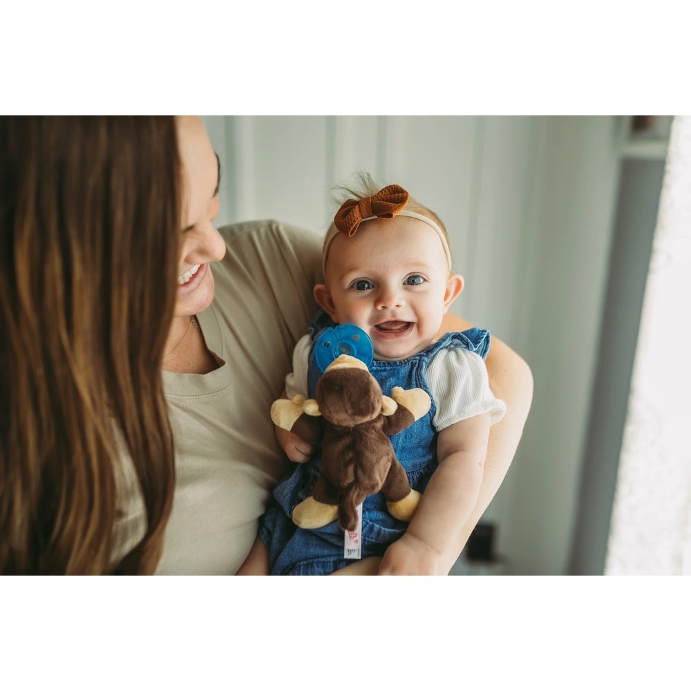 Mother cradles a smiling baby in denim, showcasing Aurora WubbaNub Infant Plush Toy Pacifier Monkey with attached pacifier.
